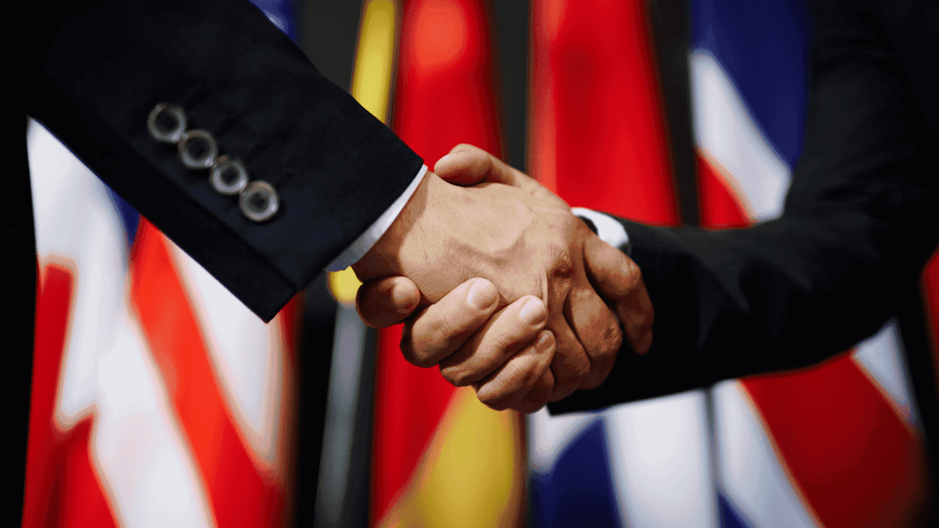 Zwei Personen beim Händedruck vor einer Reihe internationaler Flaggen, symbolisiert Zusammenarbeit und Partnerschaft.