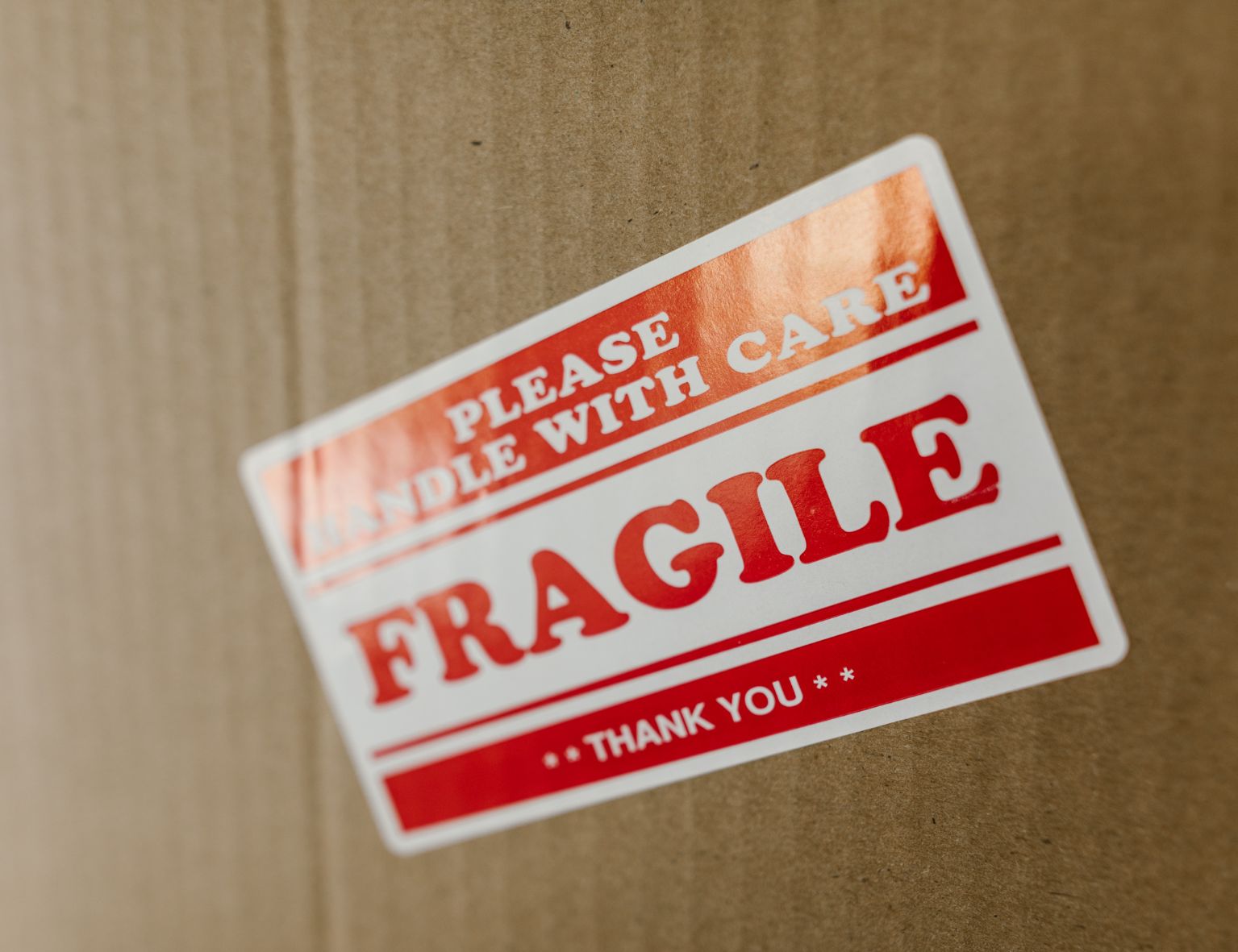 Ein brauner Versandkarton mit einem rot-weißen Aufkleber, auf dem "Bitte Vorsichtig Handhaben, Zerbrechlich, Danke" steht.