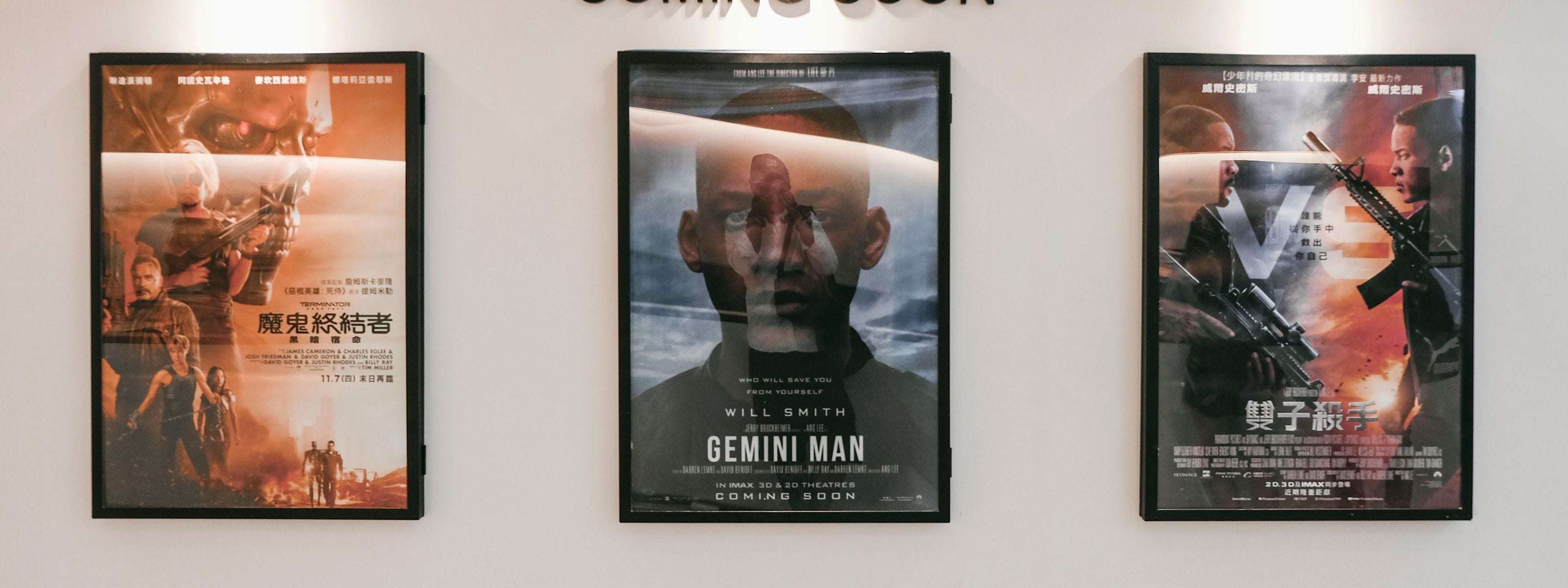 Drei gerahmte Filmplakate an einer Wand, mit Action- und Science-Fiction-Motiven, lebendigen Farben und reflektierenden Oberflächen.