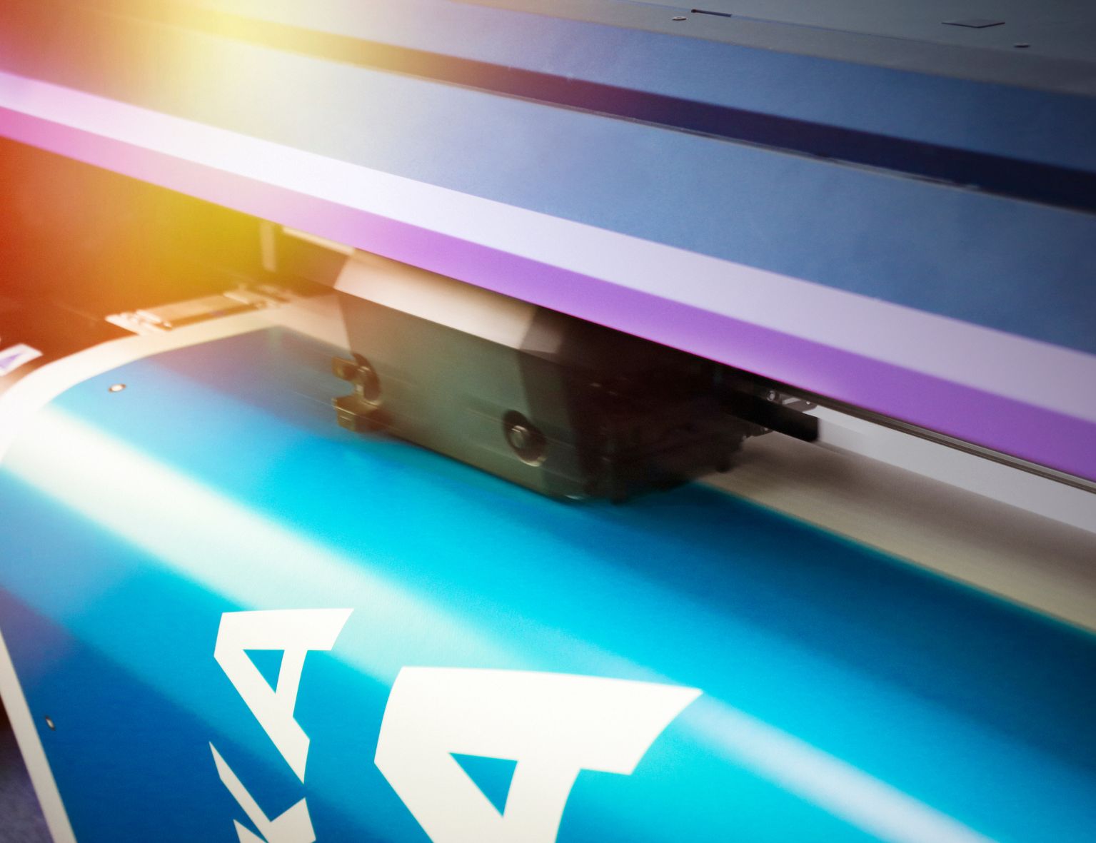 Ein Großformatdrucker in Aktion, der unter hellen Lichtverhältnissen leuchtend blaues Material mit kräftigen weißen Buchstaben bedruckt.