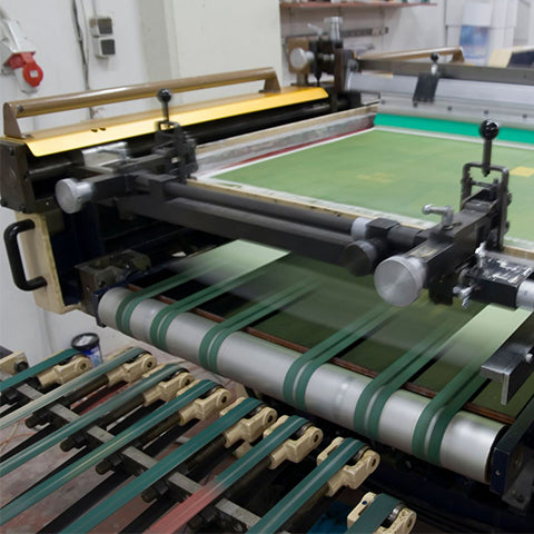 Eine Siebdruckmaschine trägt grünen Textildruck auf Material auf, mechanische Komponenten und Druckvorgang gut sichtbar.