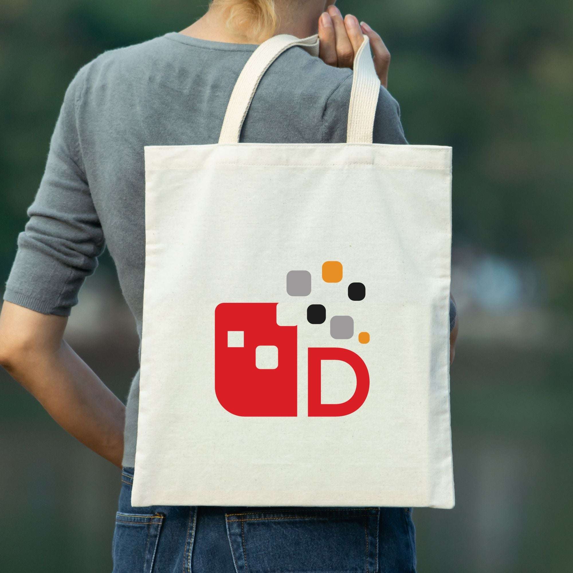 Person trägt eine Tragetasche mit buntem geometrischem Design und einem großen roten Buchstaben "D".