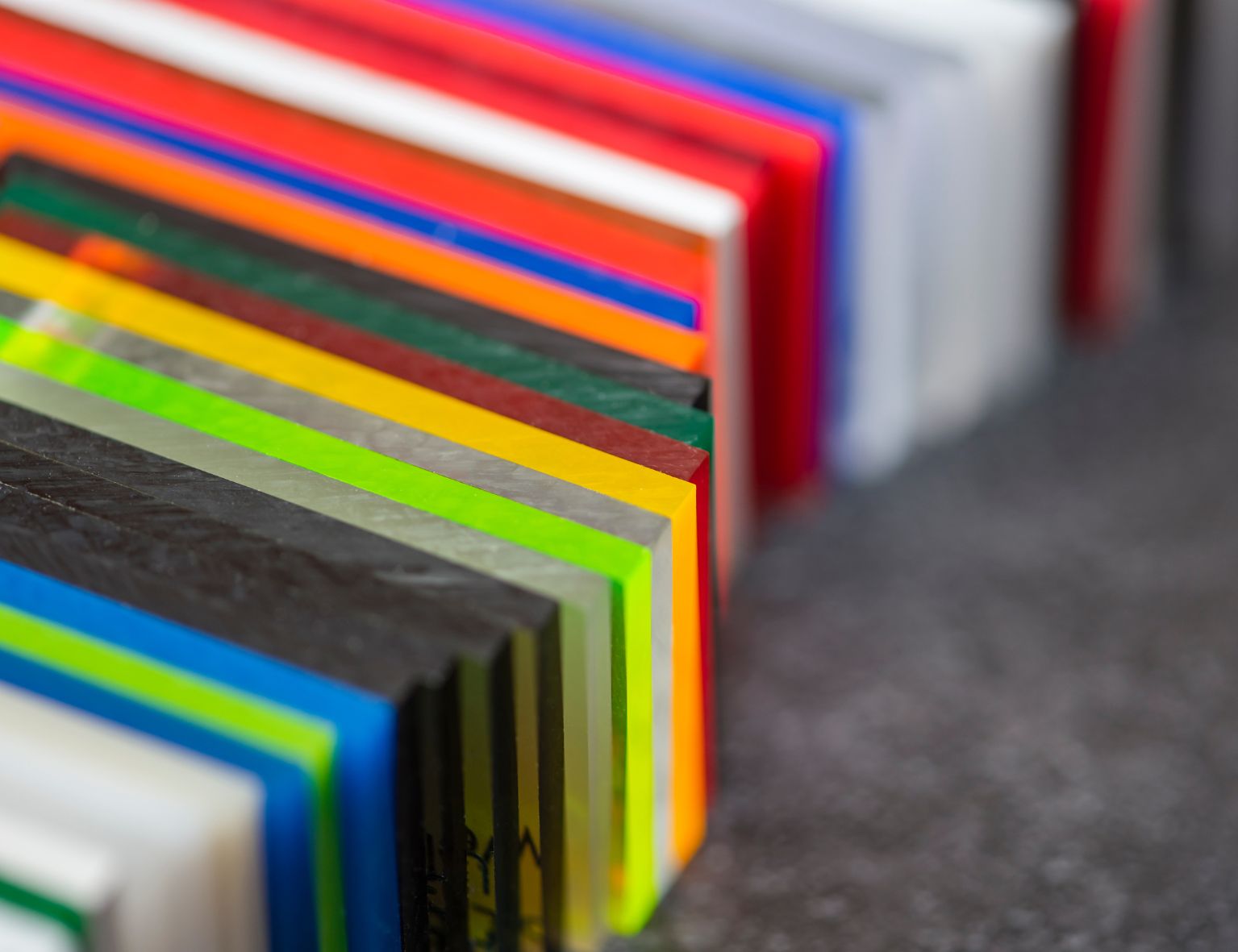 Eine Auswahl bunter Kunststoffplatten in verschiedenen Farben und Transparenzstufen, gestapelt auf einer dunklen Oberfläche.