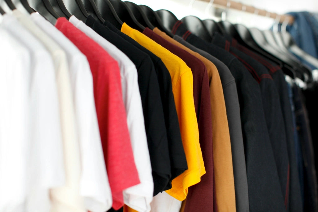 Eine Auswahl an bunten T-Shirts auf schwarzen Kleiderbügeln, ordentlich in einem Kleiderschrank arrangiert, bietet eine Vielfalt an Farben.