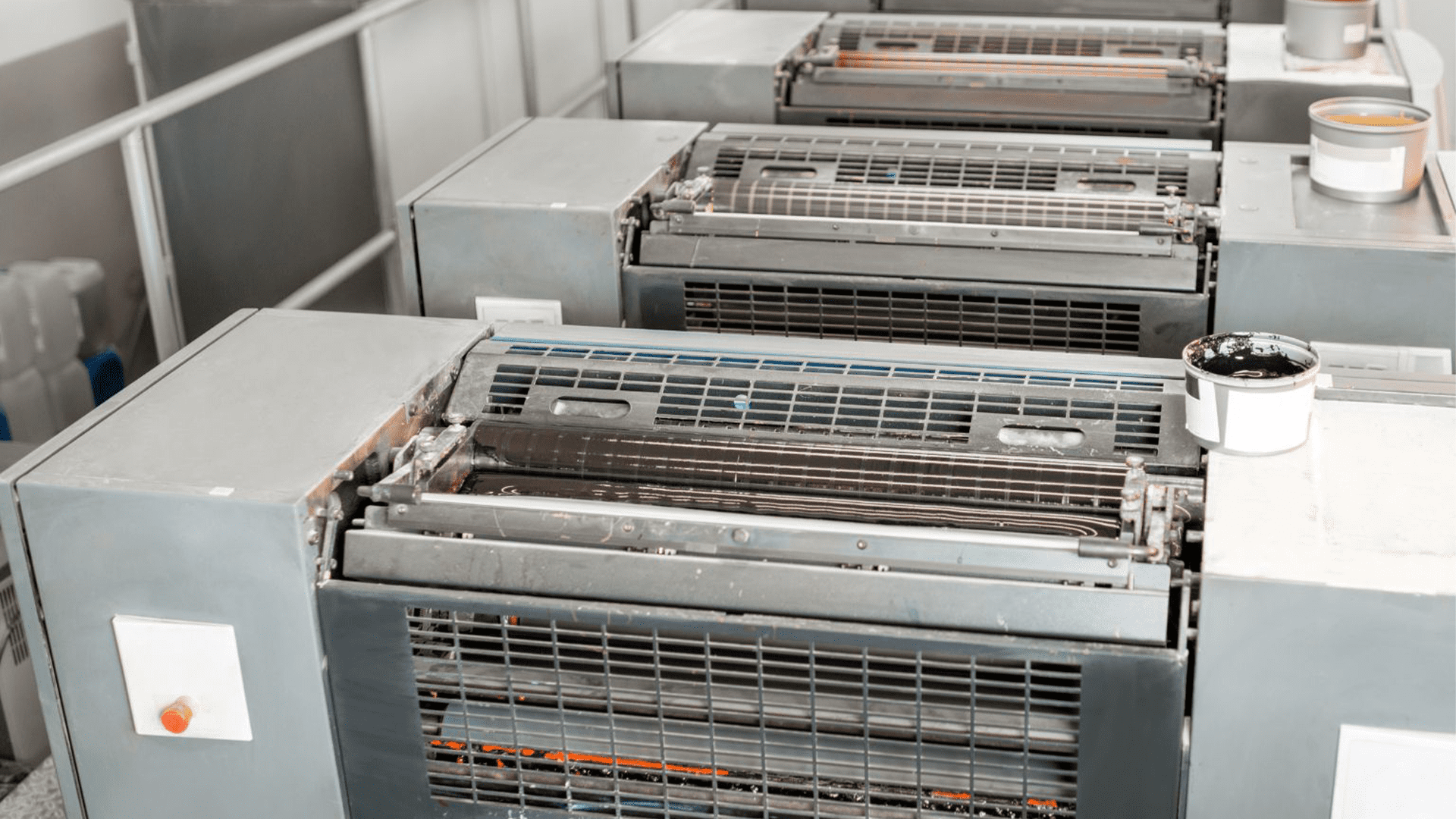 Vier industrielle Druckmaschinen in einer modernen Druckerei, zeigen Walzen und Bedienfelder, hervorhebend fortschrittliche Drucktechnologie.