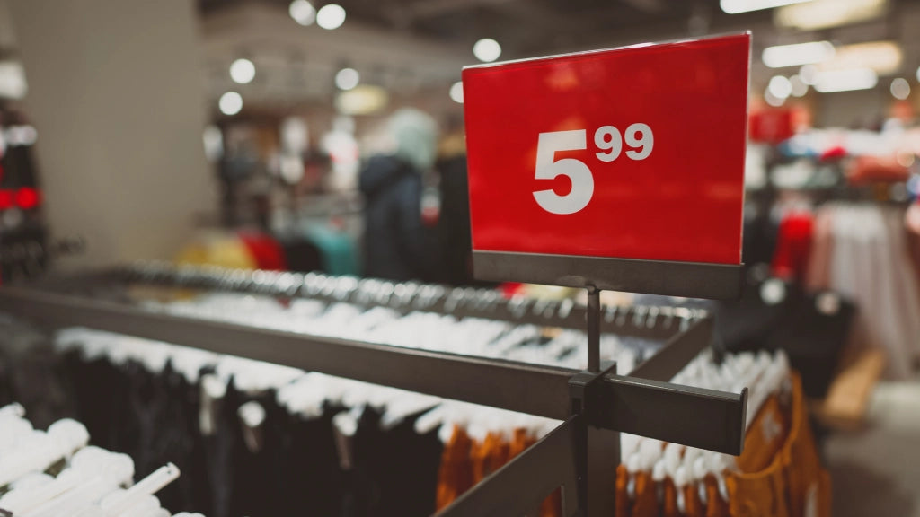 Ein rotes Preisschild in einem Bekleidungsgeschäft zeigt den Preis "5.99" in fetter weißer Schrift, was auf reduzierte Kleidung hinweist.