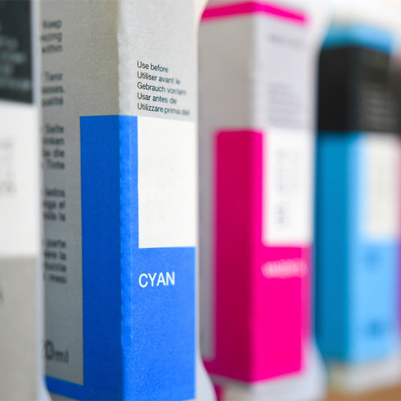 Nahaufnahme von bunten Druckertintenpatronen in Cyan-, Magenta- und Blautönen, vertikal angeordnet mit sichtbaren Textetiketten.