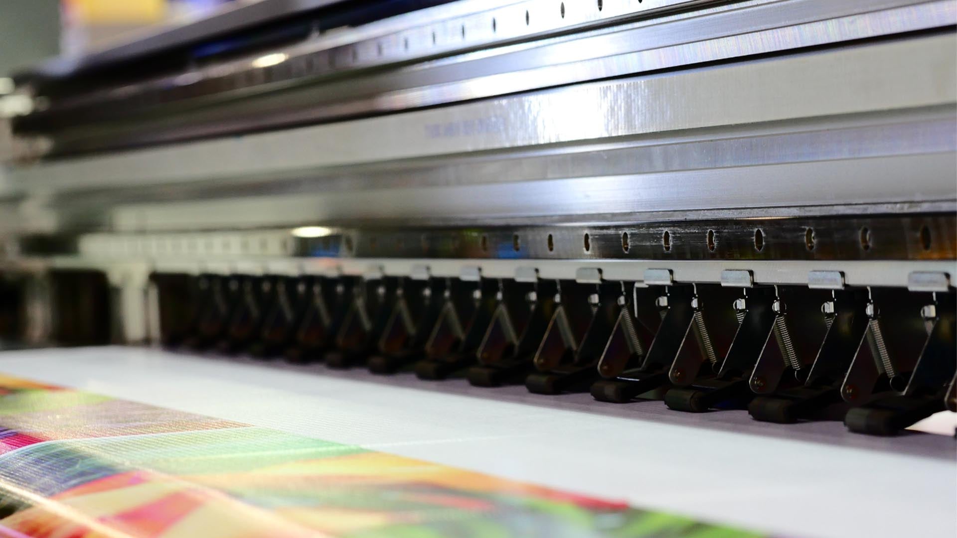 Großformatiger Farbdrucker beim Drucken farbenfroher Bilder auf Papierrolle; industrielle Druckproduktion in Aktion.