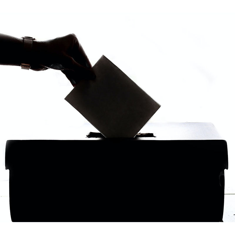 Eine Hand, die einen Umschlag in eine Wahlurne steckt, symbolisiert Abstimmung, Demokratie und bürgerschaftliches Engagement.